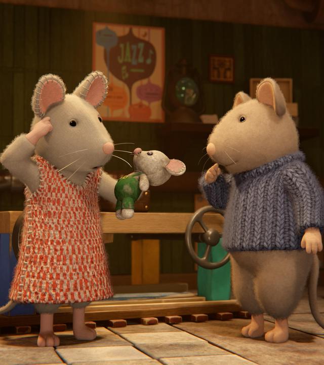 Julia und Sam stehen im Keller zwischen Regalen und Kisten. Julia hält eine kleine Stoffmaus in der linken Hand und greift sich mit der rechten Hand an die Stirn. Sam hat die rechte Hand fragend vor die Lippen gelegt. Beide schauen verwundert auf das Stofftier.