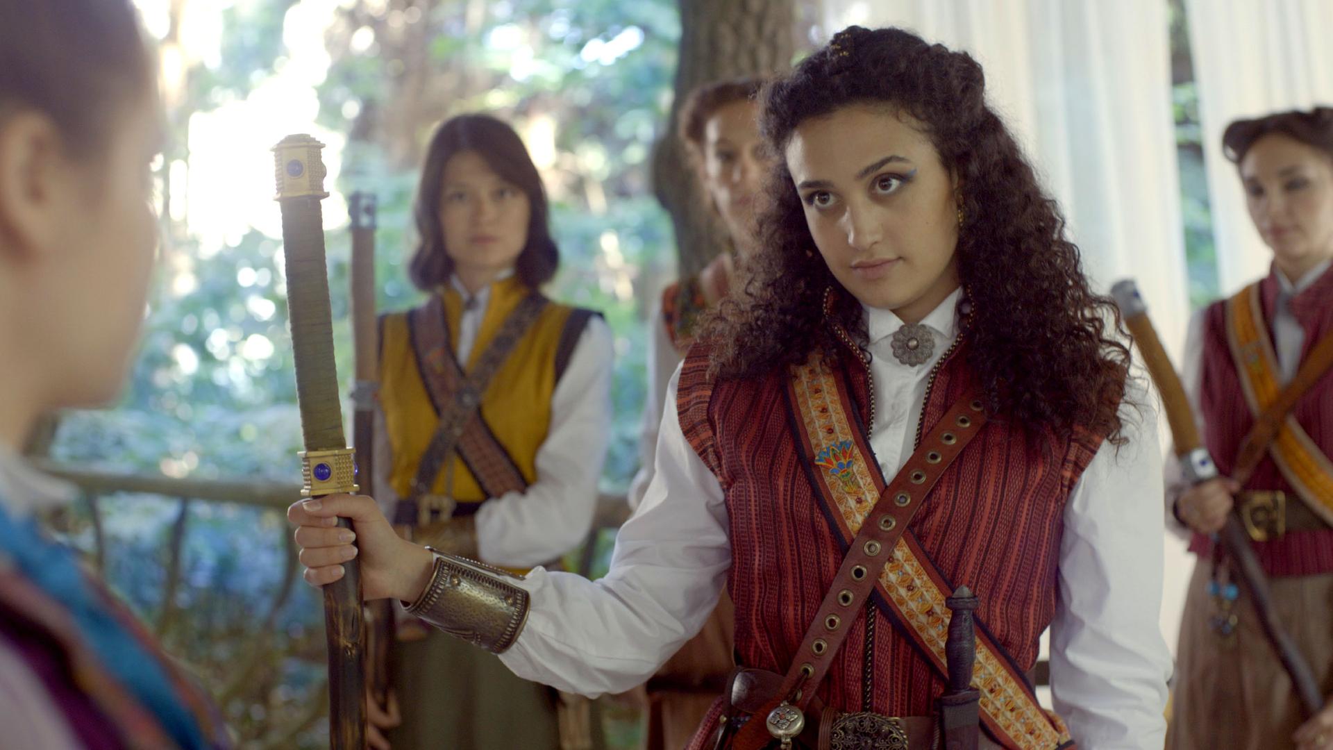 Theo trifft auf vier Mitglieder der geheimen Schwesternschaft. Sie stehen mit Schwertern bewaffnet vor ihr und sehen sie an.