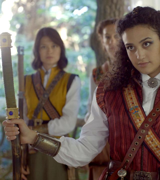 Theo trifft auf vier Mitglieder der geheimen Schwesternschaft. Sie stehen mit Schwertern bewaffnet vor ihr und sehen sie an.