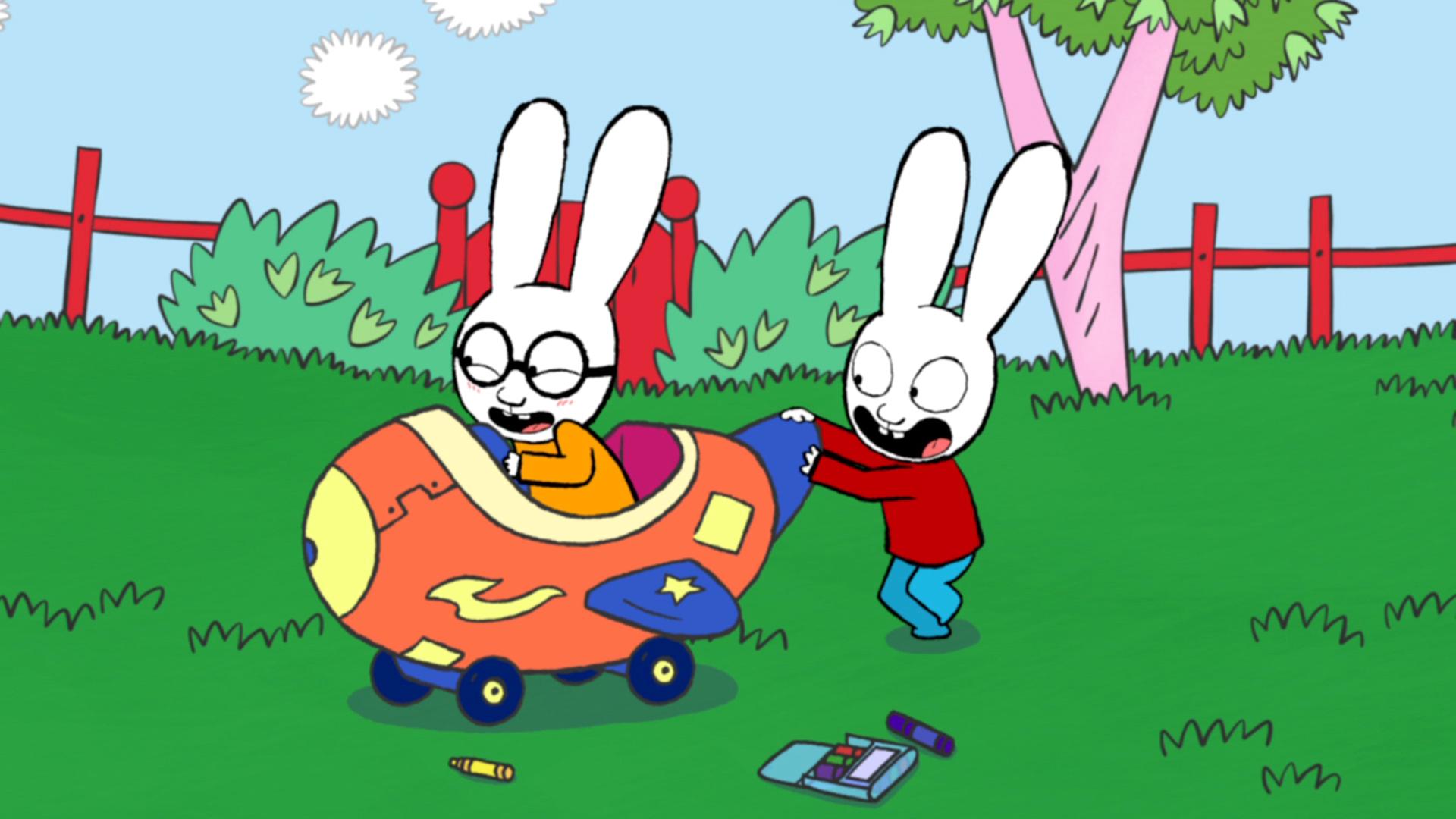 Ferdinand und Simon spielen im Garten. Ferdinand sitzt strahlend in einem von seinem Vater selbstgebauten großen Flugzeug. Simon schiebt Ferdinand und das Flugzeug fröhlich über den Rasen.