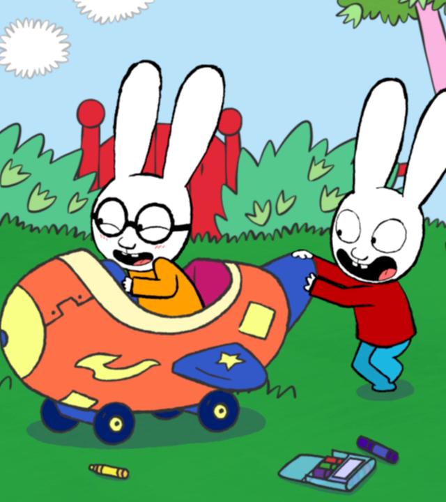 Ferdinand und Simon spielen im Garten. Ferdinand sitzt strahlend in einem von seinem Vater selbstgebauten großen Flugzeug. Simon schiebt Ferdinand und das Flugzeug fröhlich über den Rasen.