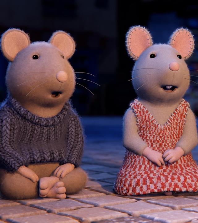 Sam und Julia hocken auf dem gepflasterten Boden und schauen aufmerksam und begeistert nach vorne. Neben ihnen sieht man die Beine von erwachsenen Hausbewohnern.