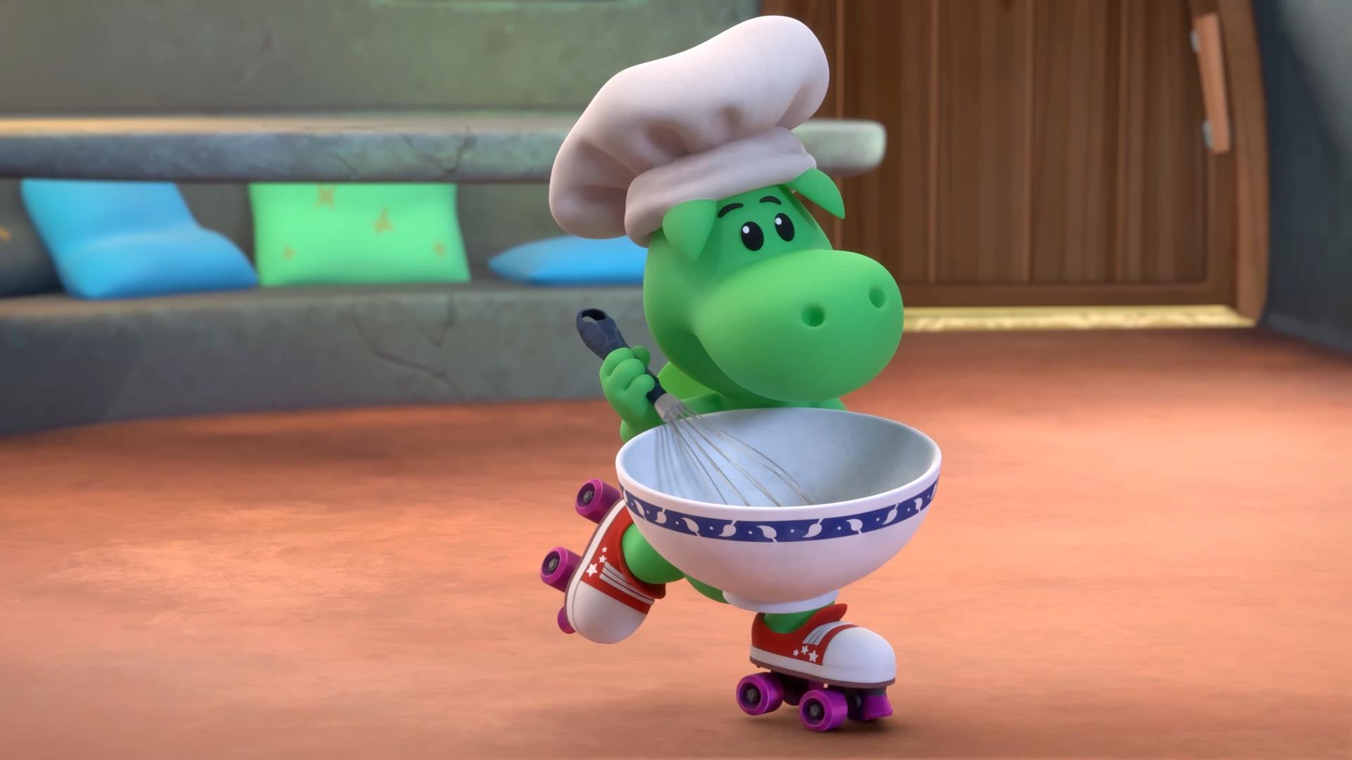 Grisu, der kleine, grüne Drache, trägt eine Kochmütze. In den Händen hält er eine Schüssel und einen Schneebesen. Er fährt auf Rollschuhen durch sein Zimmer.
