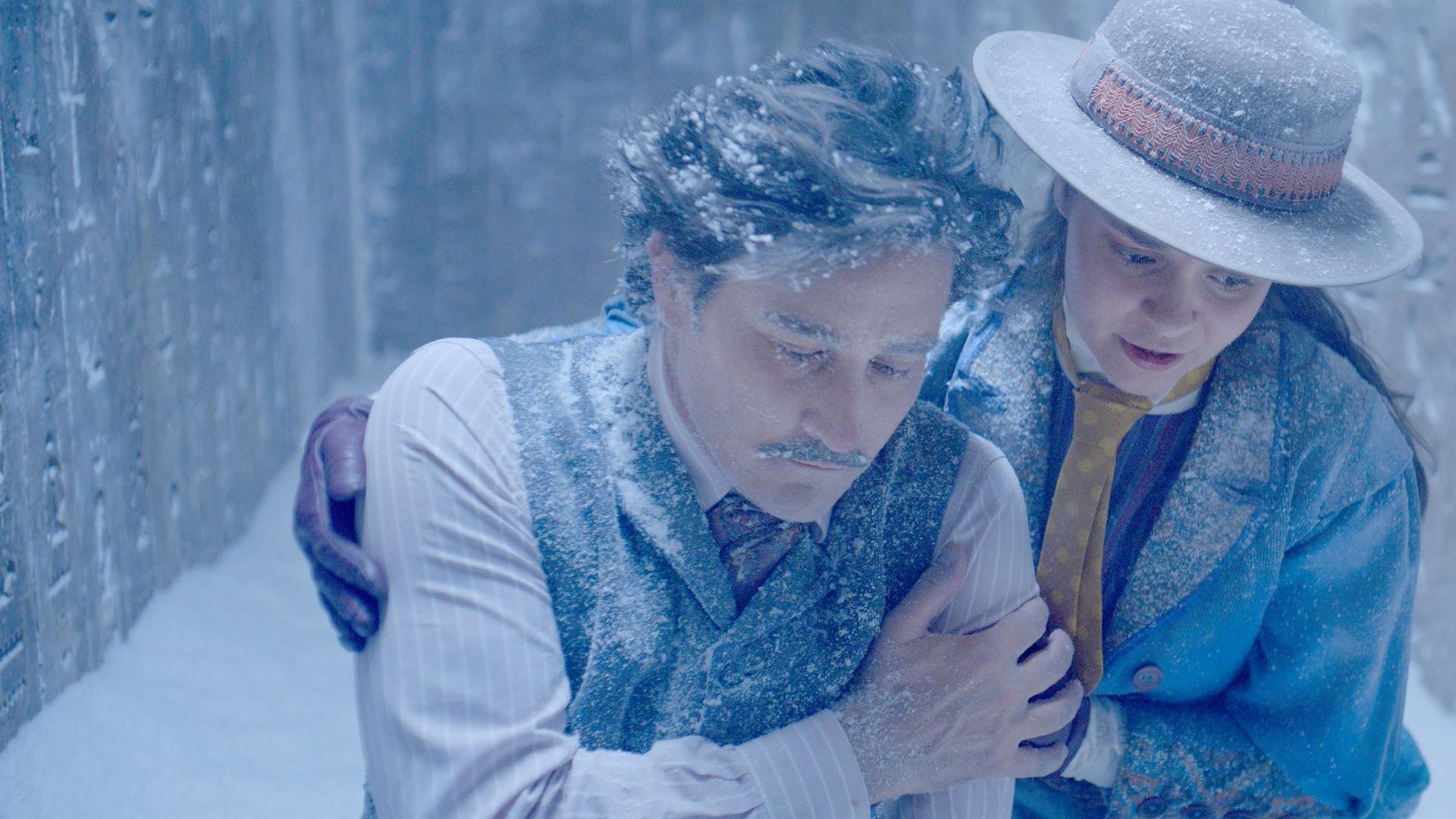 In einer alten Ruine mit Hieroglyphen an den Wänden, legt Theodosia ihrem erschöpften Vater Alistair den Arm um die Schultern. Alles ist voller Eis und beide sehen erschöpft und fast erfroren aus.