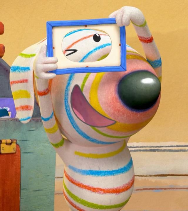 Dylan steht in der Mitte seines Wohnzimmers und hält einen kleinen Rahmen vor seine Augen. Dieser wird im Spiel wie ein Fotoapparat verwendet.