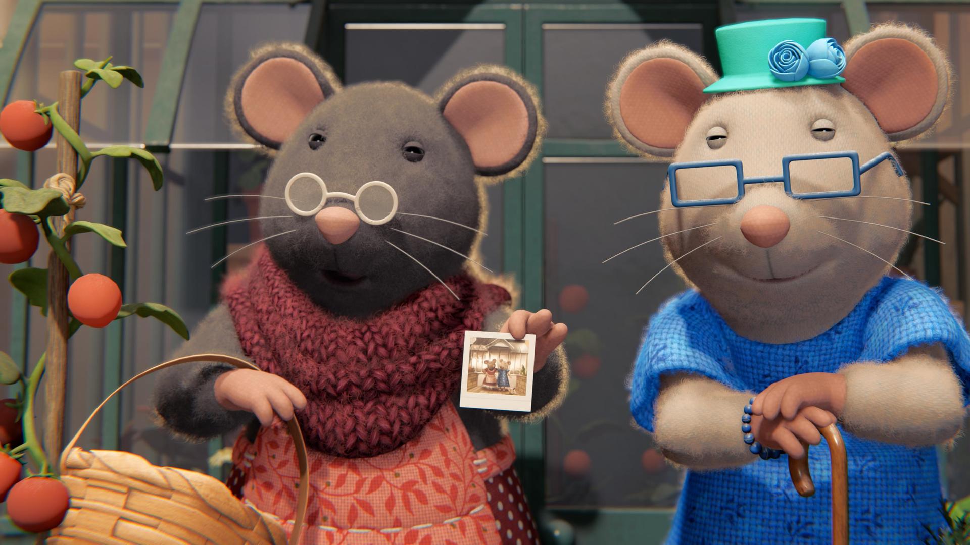 Oma Gouda und ihre alte Freundin stehen nebeneinander vor dem Gewächshaus auf der Terrasse des Mäusehauses. Oma Gouda trägt im rechten Arm einen Korb, ihre Freundin stützt sich auf einen Stock. Beide tragen Brillen und schauen zufrieden nach vorne.