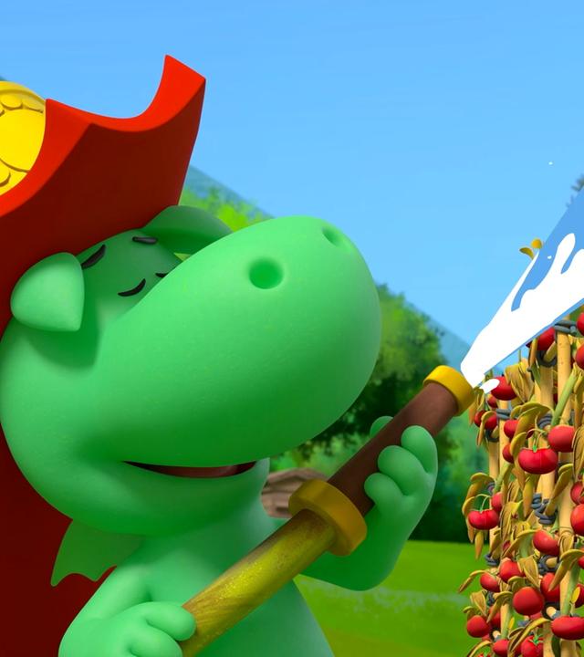 Grisu, der kleine, grüne Drache mit dem roten Feuerwehrhelm, spritzt mit einem Feuerwehrschlauch Tomaten mit Wasser nass. Er sieht dabei sehr glücklich aus und hat die Augen geschlossen.