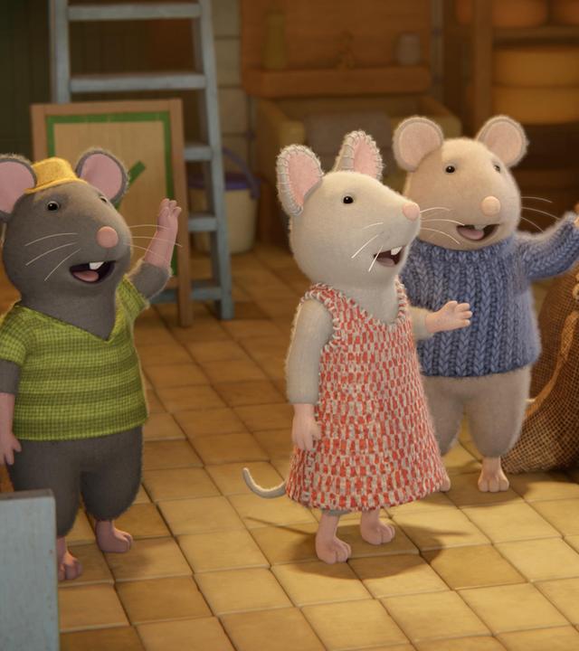 Mitten in einem Käseladen stehen Tonio, Julia und Sam und winken dem Vater von Tonio hinterher, der gerade den Laden verlässt. Um sie herum stehen mehrere Verkaufsstände mit Käsestücken. Auf einer Verkaufstheke stehen Teller mit Käse. Eine große Waage und Regale sind im Hintergrund des Ladens.