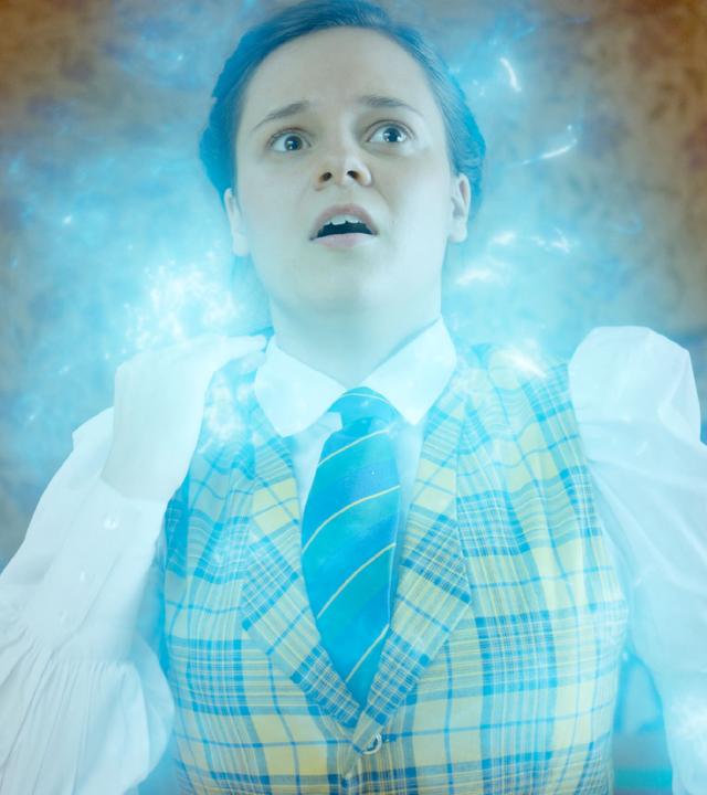 Theo ist umgeben von blau-weißem, magisch-leuchtendem Licht. Sie steht in ihrem Zimmer und sieht erschrocken aus.