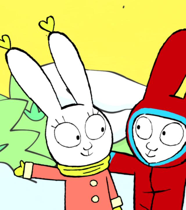 Lou, Simon und Ferdinand stehen auf dem verschneiten Pausenhof. Alle drei tragen dicke Winterjacken und Lou hat zusätzlich zwei herzförmige Ohrringe an. Simon steht in der Mitte und streckt seine Arme nach rechts und links aus, um Lou auf seiner rechten Seite und Ferdinand auf seiner linken Seite zu umarmen. Die drei Freunde lachen gemeinsam und strahlen sich an.