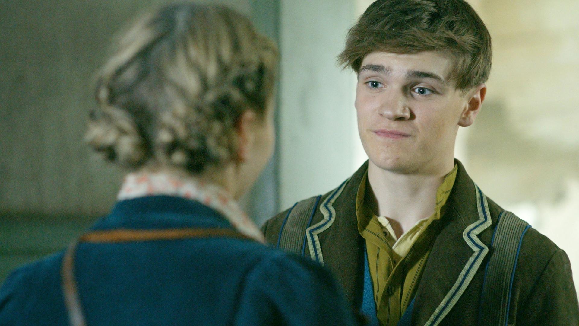 Henry schaut etwas verzweifelt auf Maya, von der wir nur den Rücken und ihre geflochtenen Haaren sehen.