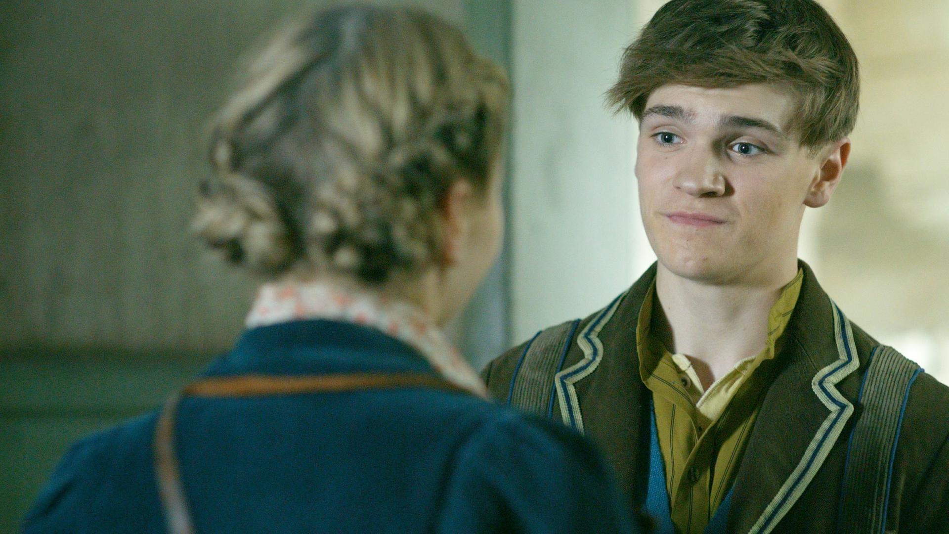 Henry schaut etwas verzweifelt auf Maya, von der wir nur den Rücken und ihre geflochtenen Haaren sehen.