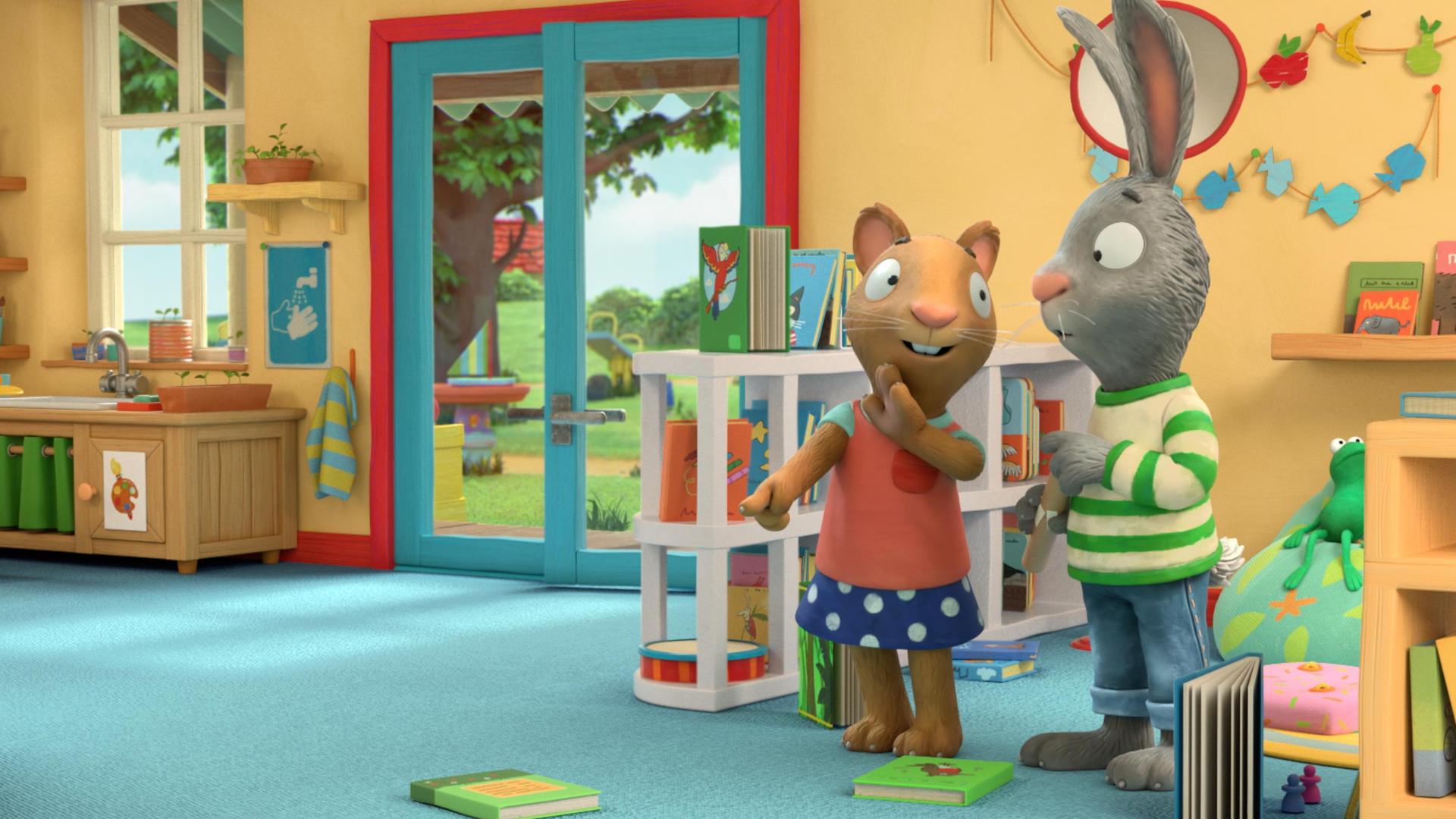 Die Maus Posy zeigt auf eins der Bücher, die verteilt auf dem Teppichboden liegen und sagt etwas zu ihrem Freund Pip, der neben ihr steht. Pip, das Kaninchen blickt etwas ratlos.