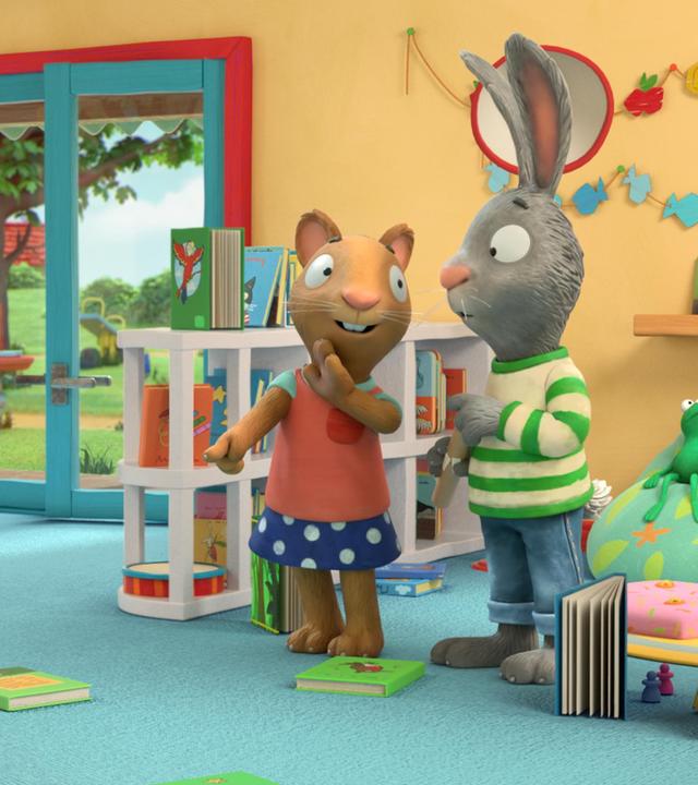 Die Maus Posy zeigt auf eins der Bücher, die verteilt auf dem Teppichboden liegen und sagt etwas zu ihrem Freund Pip, der neben ihr steht. Pip, das Kaninchen blickt etwas ratlos.
