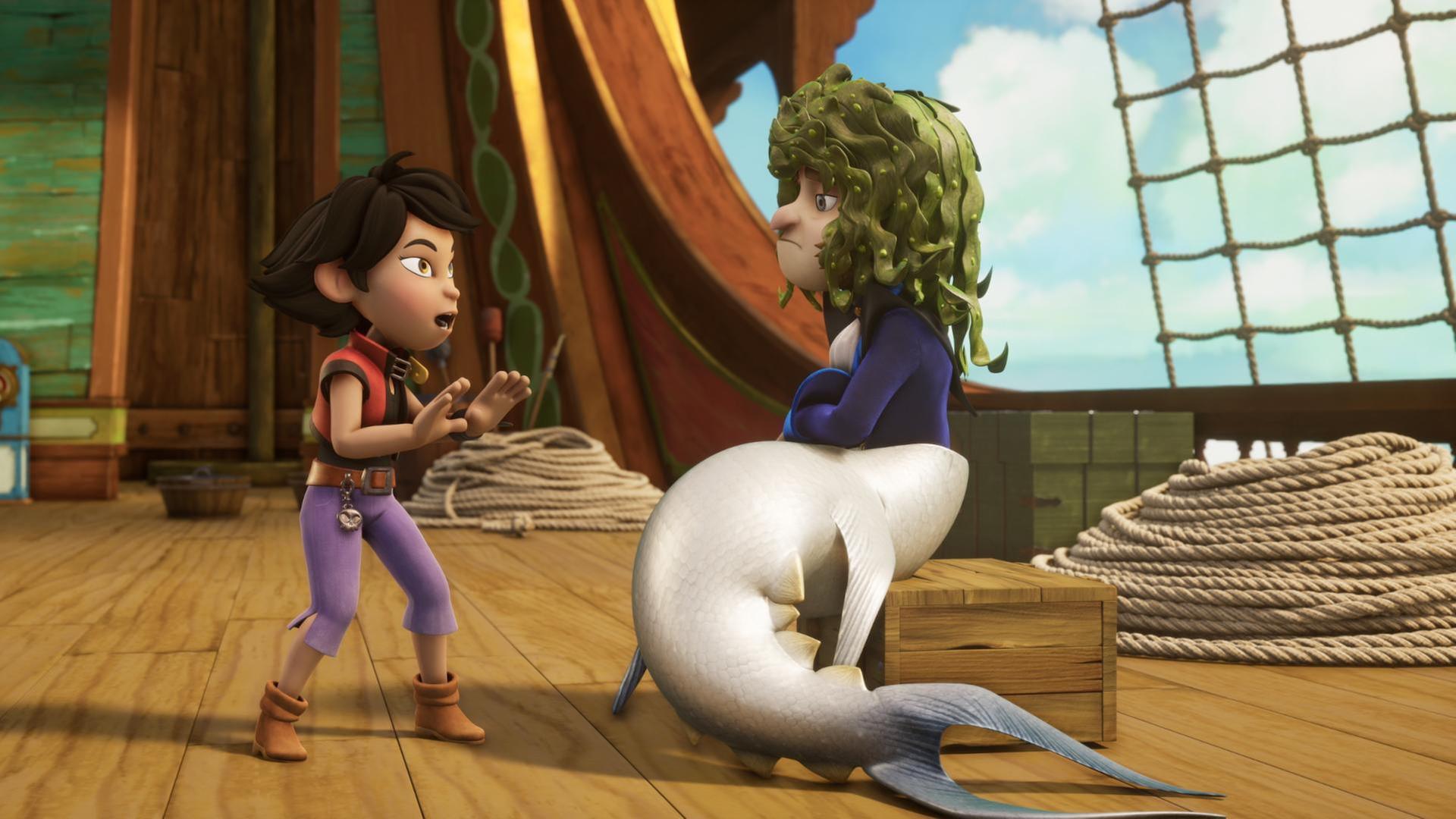 Käpt'n Flint sitzt als Meerjungfrau verkleidet auf einer Holzkiste. Er hat eine Haiflosse an und Meeralgen als Perücke auf seinem Kopf. Vor ihm steht Zoe und hält in einer Abwehrhaltung mit ihrem Händen nach vorne.