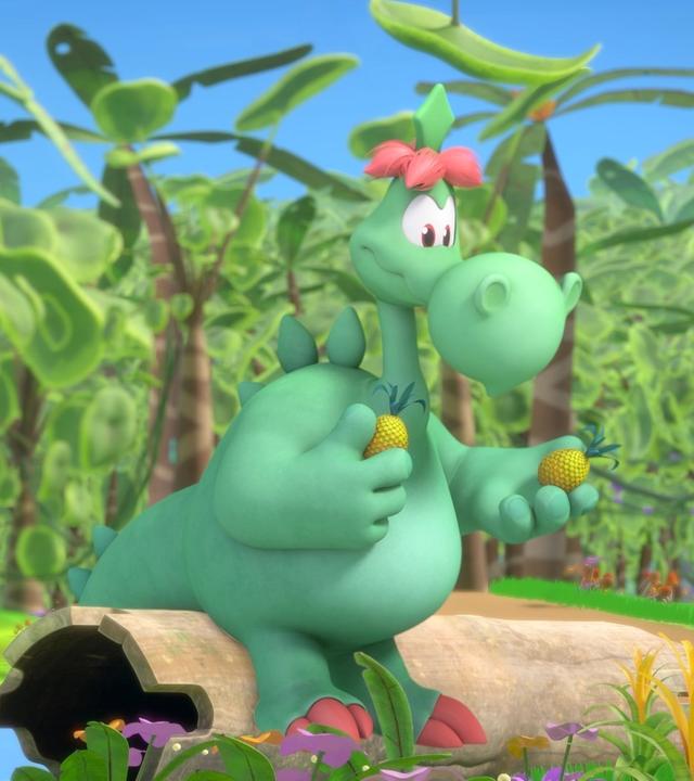 Grisu, der kleine Drache, und sein Vater Fumé sind im Urwald. Grisu betätigt eine Filmkamera, die auf einem Stein vor ihm liegt. Fumé sitzt etwas abseits auf einem Baumstumpf und hält Ananas in den Händen.