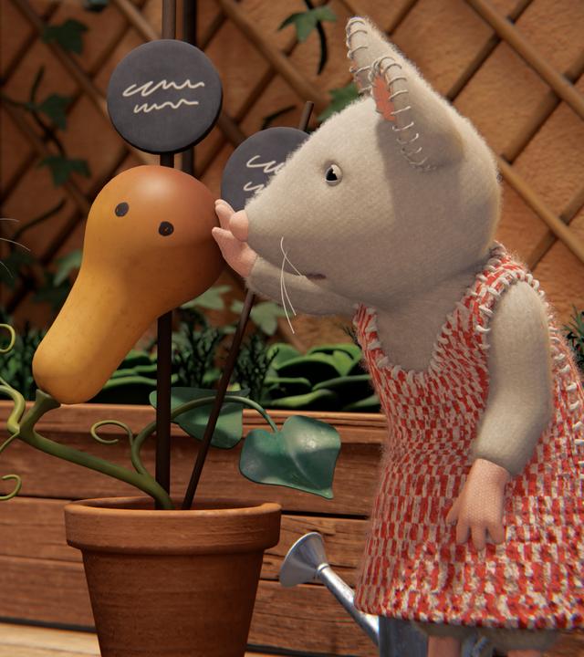 Sam und Julia stehen auf der Terrasse zwischen Hochbeeten und betrachten von beiden Seiten einen Kürbis, der in einem Topf gewachsen ist. Er hat zwei runde Flecken, die wie Augen aussehen, und Julia tätschelt liebevoll den Kürbis-Kopf.