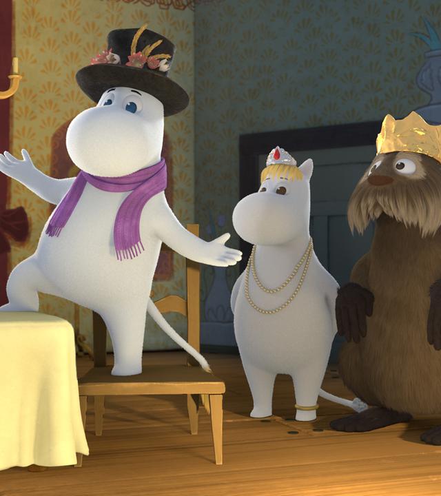 Muminpapa trägt einen lila Schal um den Hals und steht mit einem Bein auf dem Küchentisch, mit dem anderen auf einem Stuhl. Zusammen mit Snorfräulein und Otter steht er auf einer Theaterbühne und schauspielt.