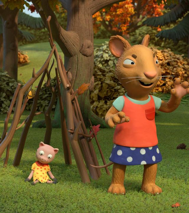 Im Park steht die Maus Posy, fies und grimmig blickend mit gefährlich erhobenen Händen vor einem aus Stöcken gebauten Kerker. Darin sitzt das Kuscheltier Schweinchen. Die Laubbäume sind herbstlich gefärbt.