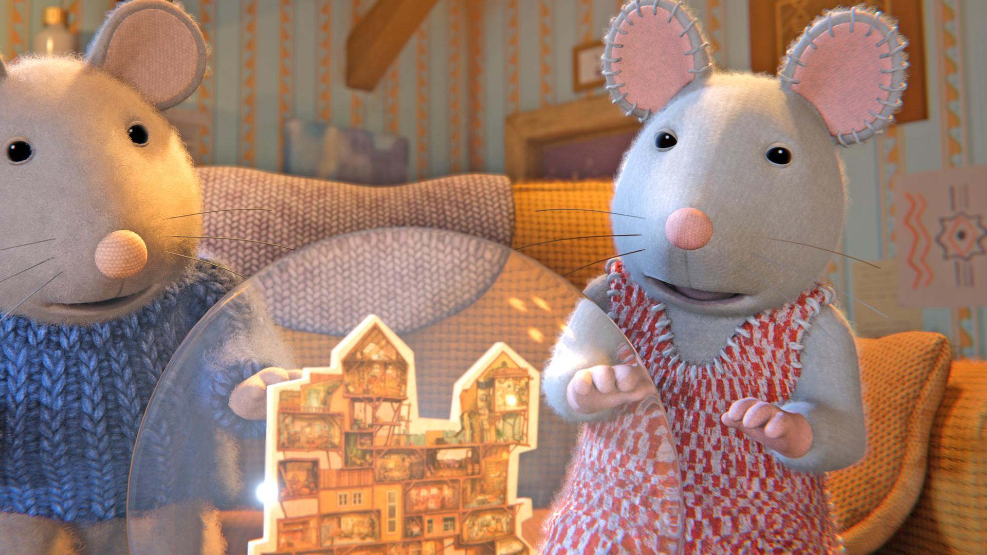 Sam und Julia sitzen auf einem Sofa in einem Zimmer mit gestreifter Tapete. Sie schauen hoffnungsvoll auf ein Modell des Mäusehauses in einer Schneekugel.