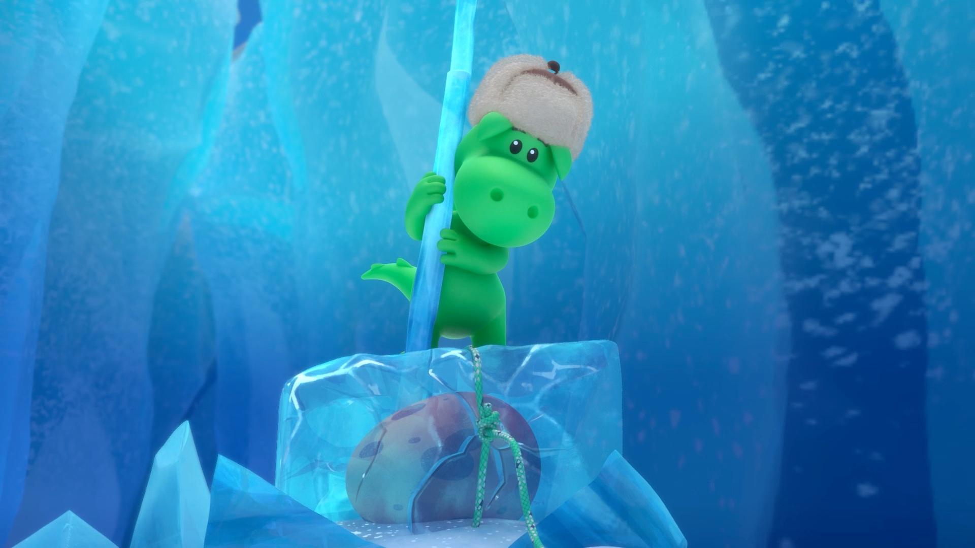 Grisu, der kleine, grüne Drache trägt eine warme Wintermütze. Er steht auf einem Eisblock in einer Gletscherspalte. Im Eisblock eingeschlossen ist ein Ei.