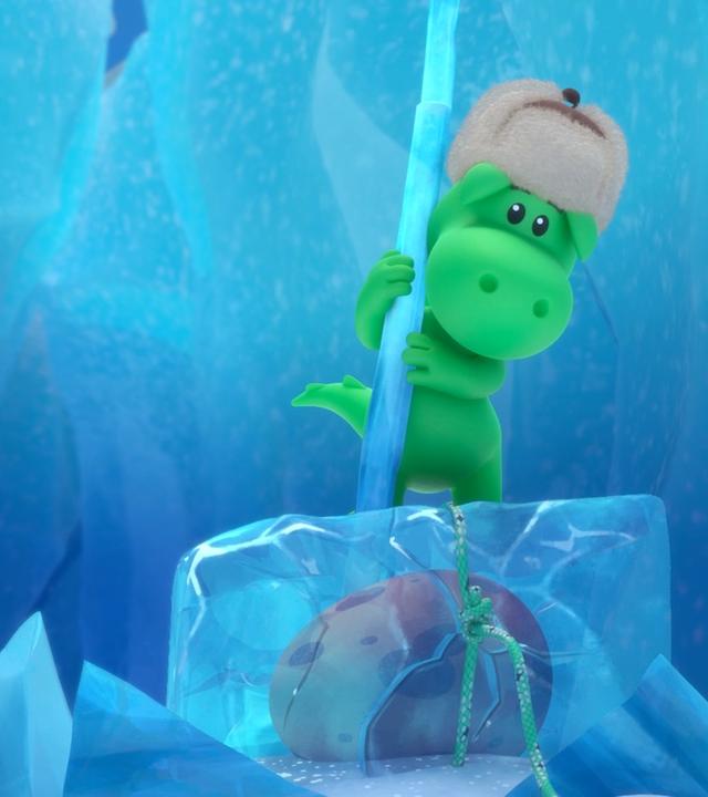 Grisu, der kleine, grüne Drache trägt eine warme Wintermütze. Er steht auf einem Eisblock in einer Gletscherspalte. Im Eisblock eingeschlossen ist ein Ei.