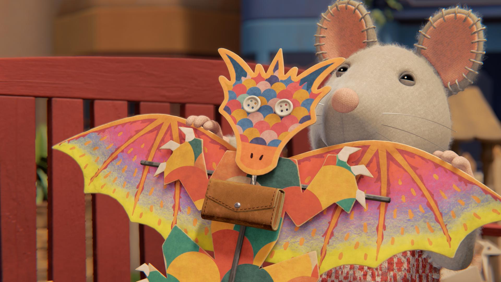 Julia steht draußen und hält einen bunten, selbstgebastelten Flugdrachen vor sich. Er hat auf dem Bauch eine kleine Ledertasche mit einem Verschluss.