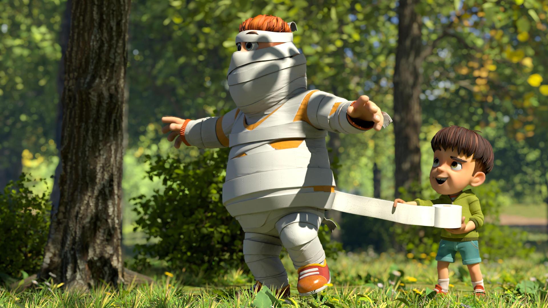 Im Wald hilft Kleiner Fuß Samson lachend dabei, sich in eine Mumie zu verwandeln. Er ist von Kopf bis Fuß schon mit Toilettenpapier eingewickelt und Kleiner Fuß wickelt gerade weitere Bahnen um ihn. Samson hält seine Arme weit vom Körper ausgestreckt.