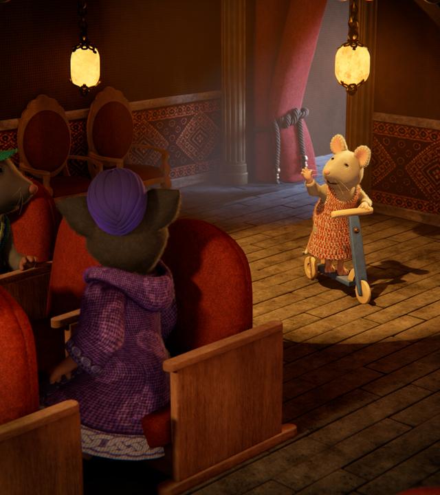 Julia steht mit ihrem Roller auf der Theaterbühne im Scheinwerferlicht und hebt grüßend den Arm. Das Publikum schaut auf sie.