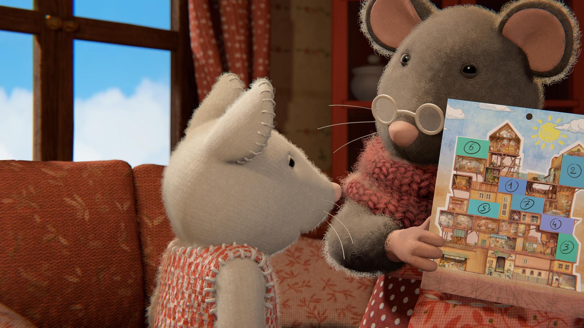 Oma Gouda hält einen Kalender in den Händen und zeigt ihn Julia, die vor ihr steht. Auf dem Vorderblatt des Kalenders ist das Mäusehaus abgebildet. Oma Gouda spricht zu Julia, die aufmerksam den Kalender betrachtet. Hinter den beiden steht eine Couch vor einem Fenster.