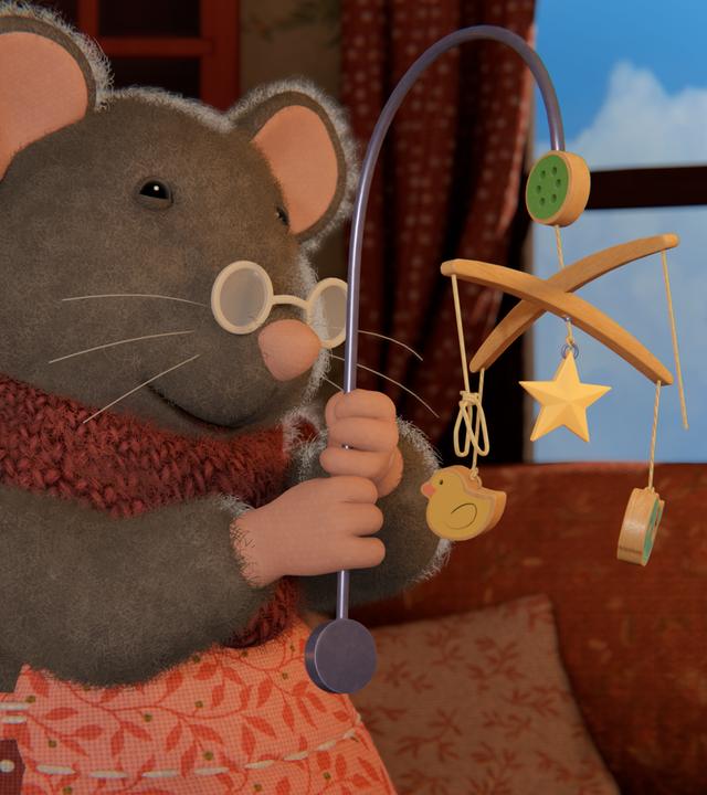 Oma Gouda hält mit beiden Händen das alte Mobile mit den vielen kleinen Holzteilchen in verschiedenen Formen hoch und betrachtet es.