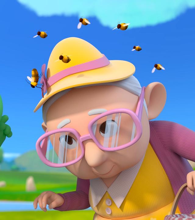 Grisu, der kleine grüne Drache mit dem roten Feuerwehrhelm, zeigt auf herumfliegende Bienen. Die Bienen schwirren um den Hut von Oma Gertrud herum. Oma Gertrud ist eine ältere Dame mit gelbem Hut und rosafarbener Brille.