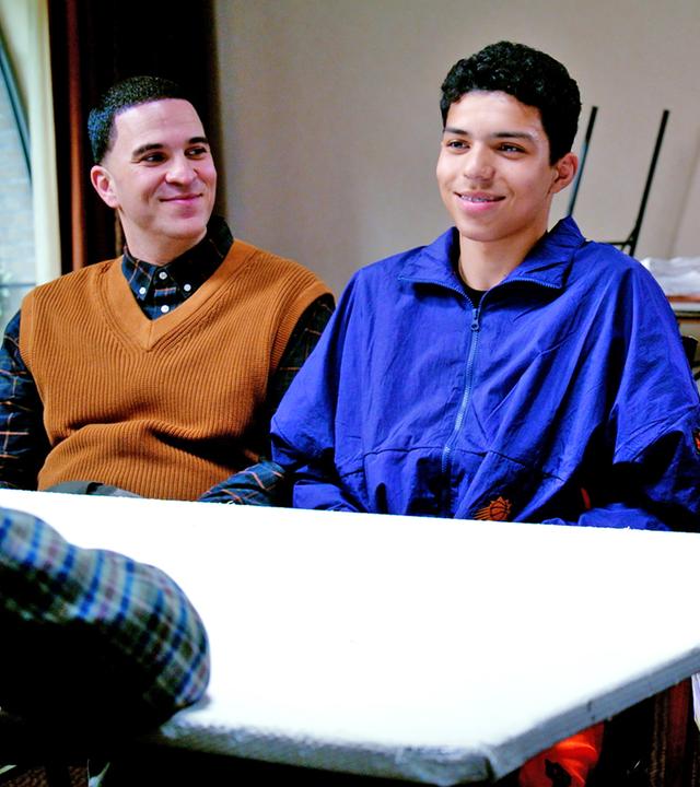 Im Klassenzimmer sitzen Omar und seine Eltern dem Lehrer gegenüber an einem Tisch. 