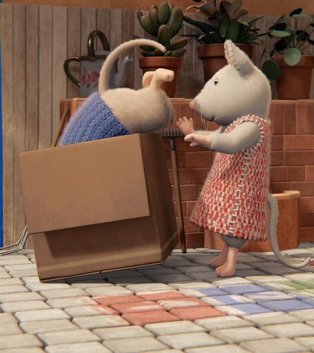 Julia hilft Sam, sich in einem Karton zu verstecken. Sam ist schon mit dem Oberkörper darin verschwunden. Nur sein Hinterteil mit dem Mäuseschwanz schaut noch heraus.