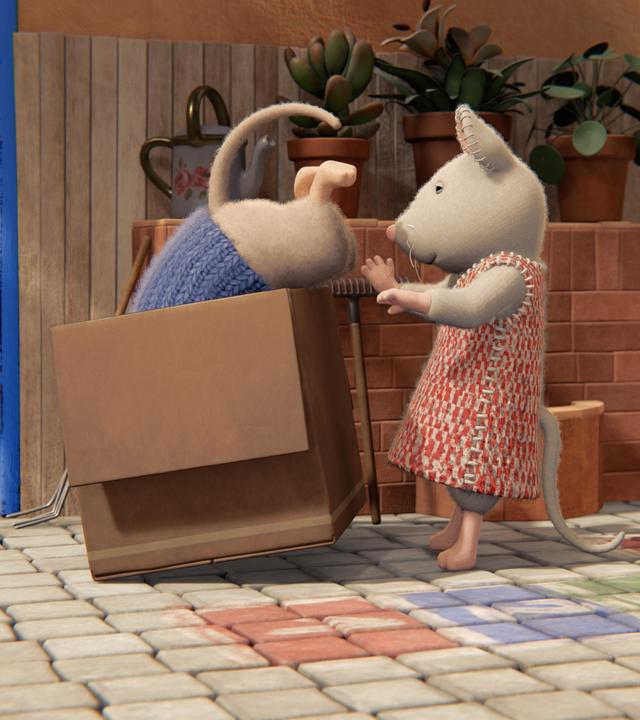 Julia hilft Sam, sich in einem Karton zu verstecken. Sam ist schon mit dem Oberkörper darin verschwunden. Nur sein Hinterteil mit dem Mäuseschwanz schaut noch heraus.