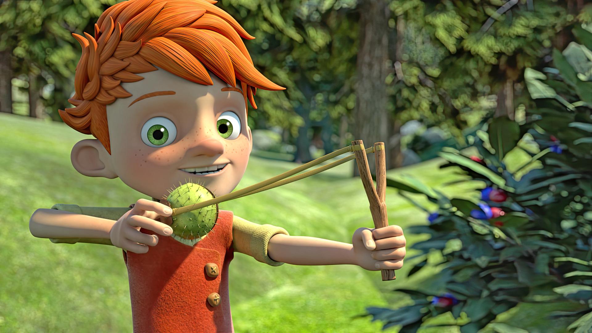 Yuki steht frech grinsend im Wald und hält eine Schleuder in der Hand, in die er eine Kastanie eingespannt hat, die sich noch in ihrer stacheligen grünen Schale befindet.