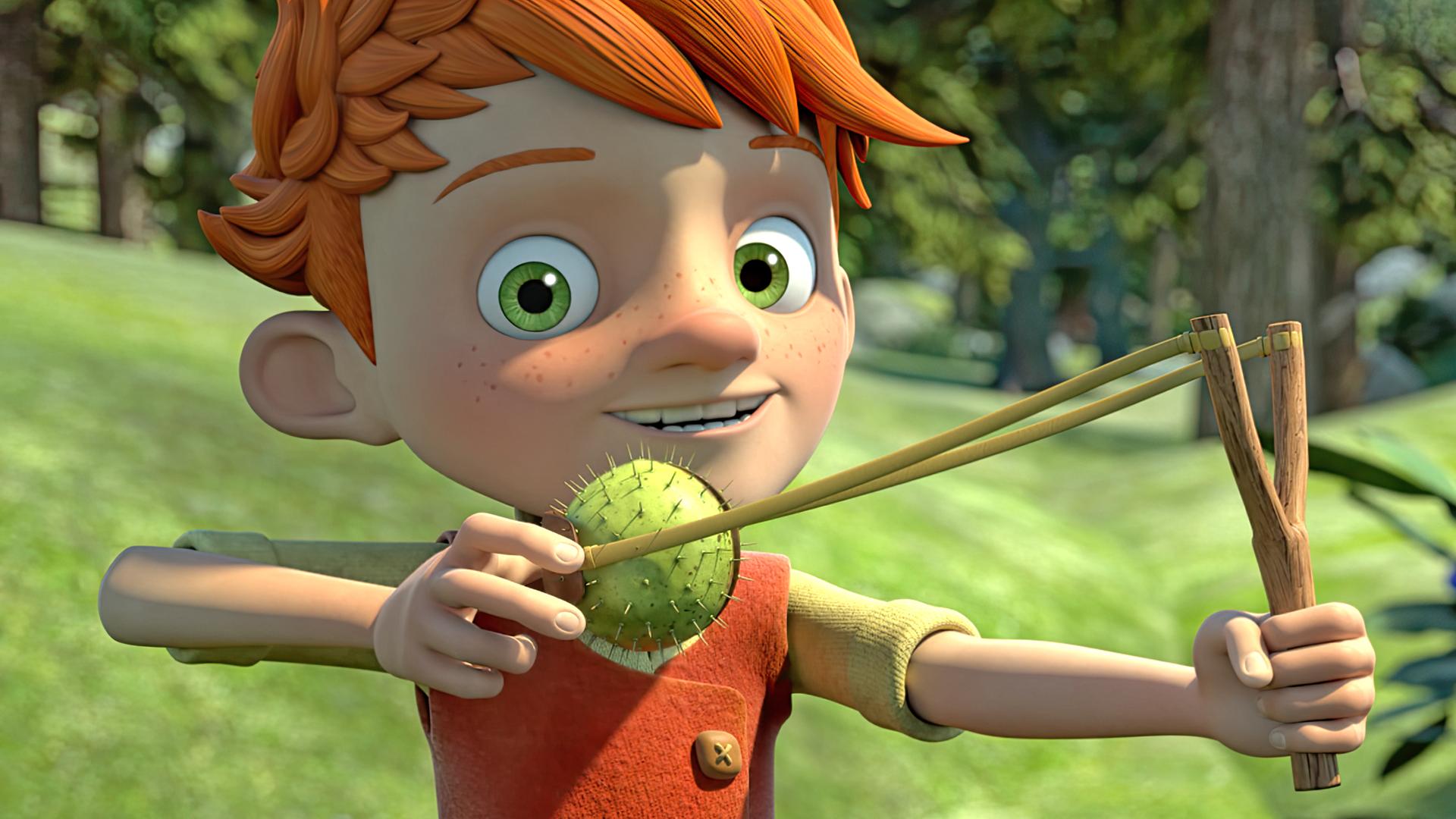 Yuki steht frech grinsend im Wald und hält eine Schleuder in der Hand, in die er eine Kastanie eingespannt hat, die sich noch in ihrer stacheligen grünen Schale befindet.