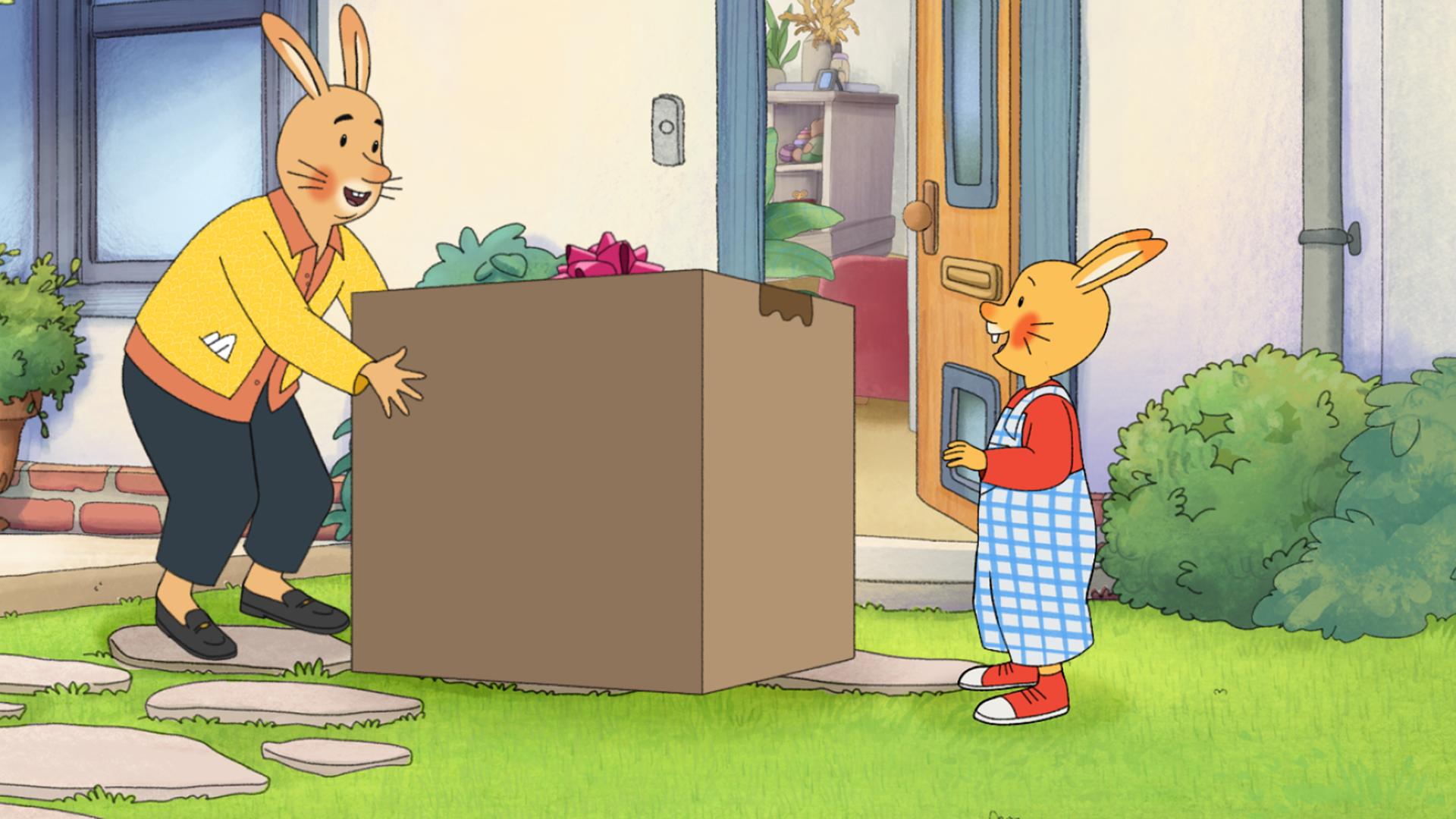 Vor einem Haus mit offener Eingangstür steht ein großes, quadratisches Paket aus Karton. Neben dem Paket stehen Karlchen und die Empfängerin, Monikas Mama.