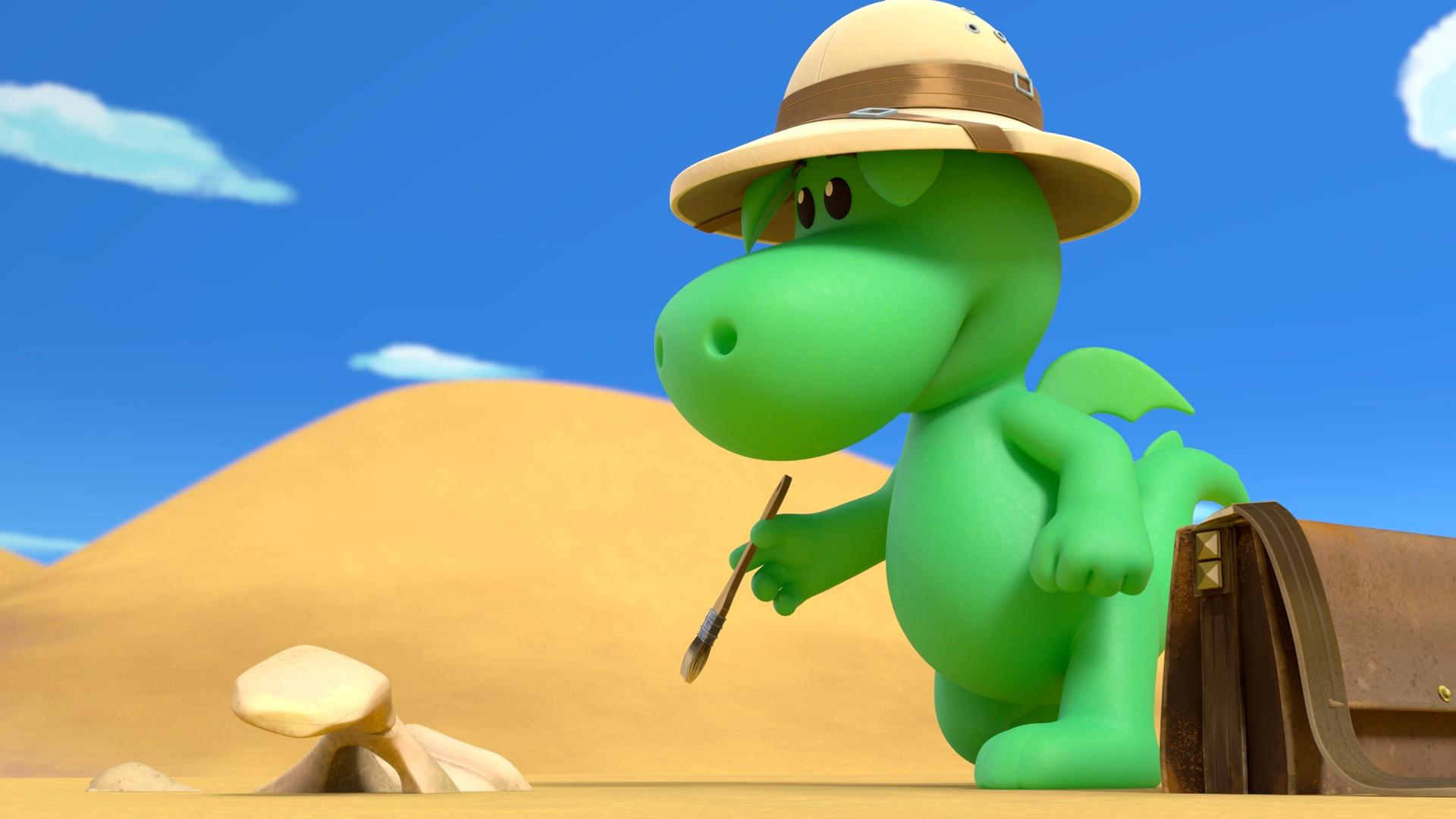Grisu, der kleine grüne Drache, steht mit einem Tropenhut in der Wüste. Er hat einen kleinen Pinsel in der Hand, vor ihm im Wüstensand liegt ein Knochen.