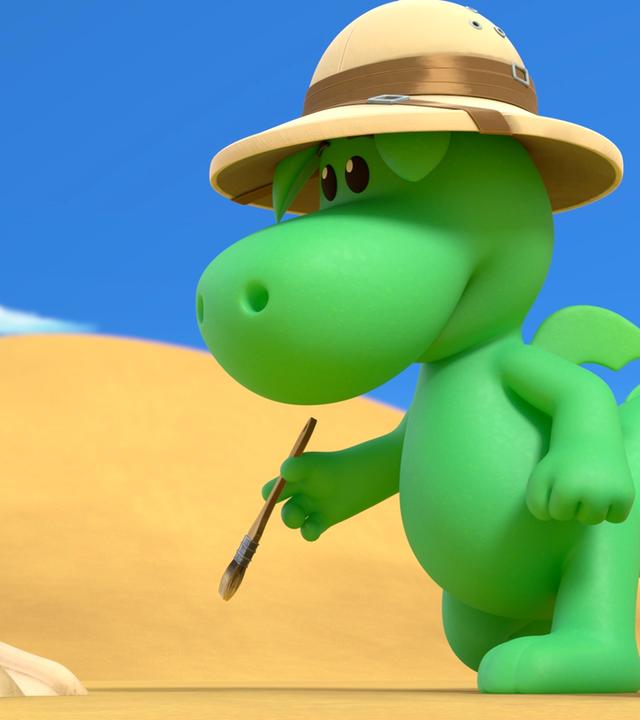 Grisu, der kleine grüne Drache, steht mit einem Tropenhut in der Wüste. Er hat einen kleinen Pinsel in der Hand, vor ihm im Wüstensand liegt ein Knochen.