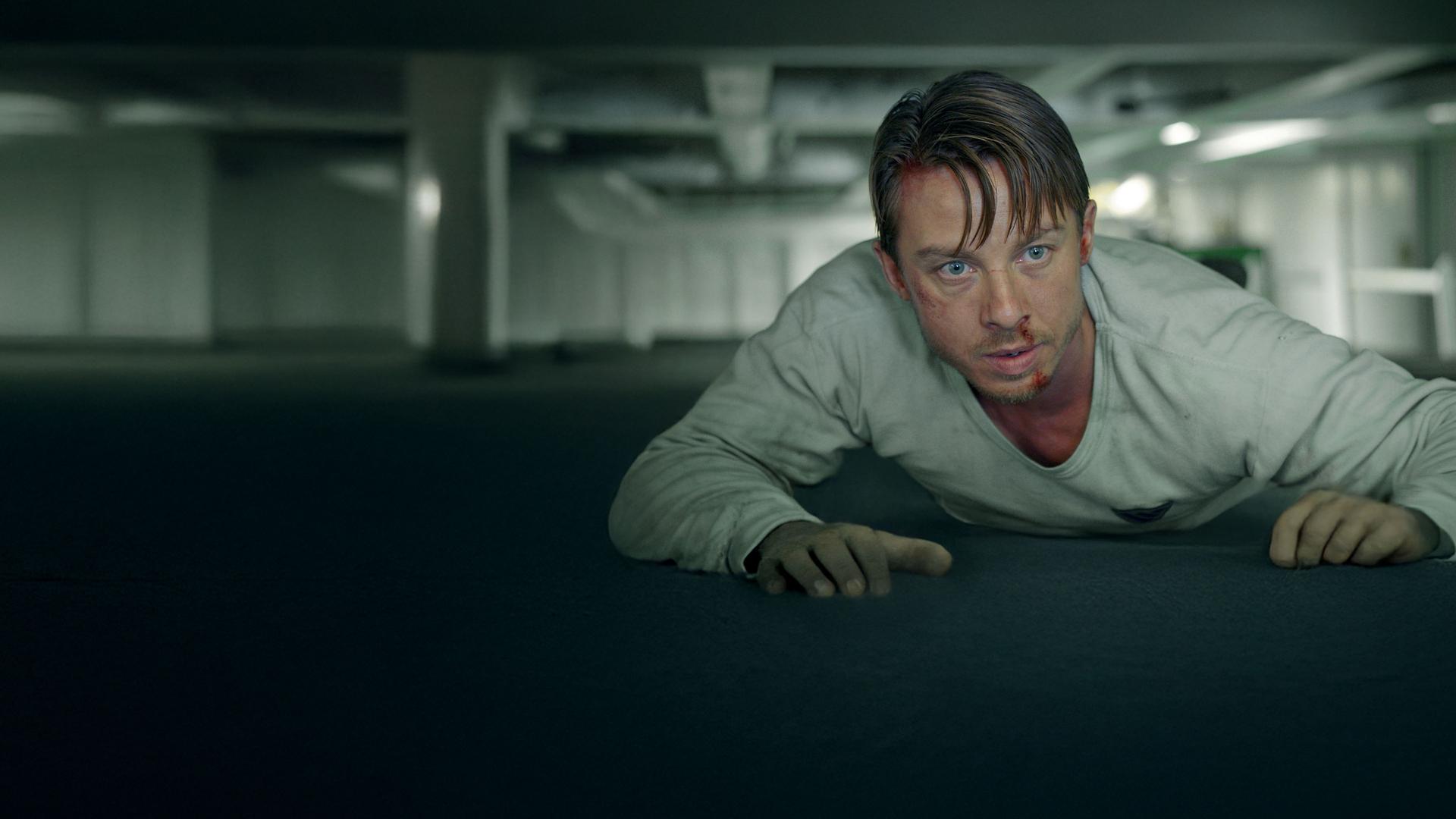 Philip Nørgaard (Johannes Lassen) liegt auf einem Container in einem Frachtraum und schaut unruhig in Richtung Kamera.