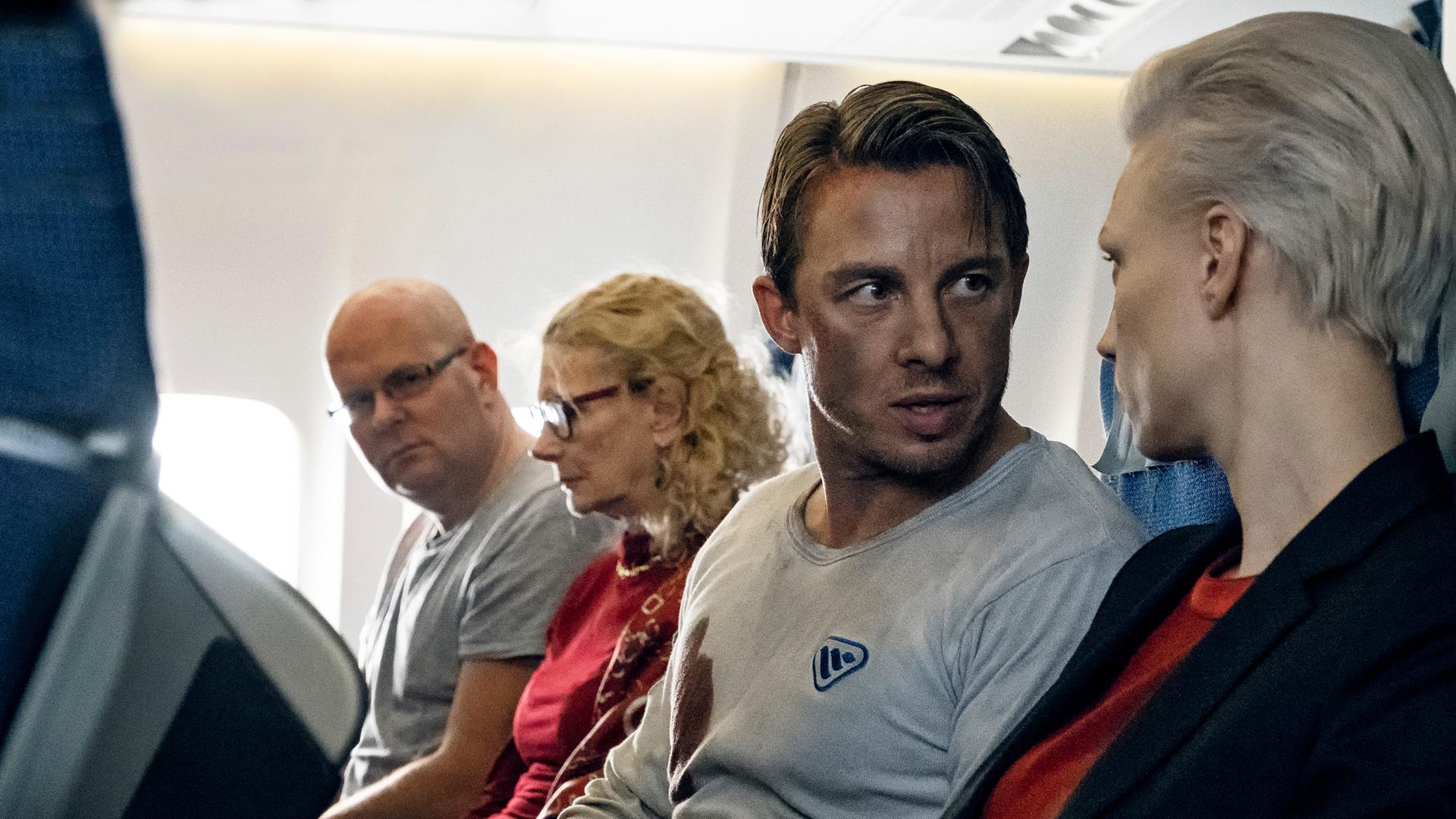 Philip (Johannes Lassen) spricht mit Anna Kasharina (Lise Risom Olsen). Die beiden sitzen im Flugzeug nebeneinander.