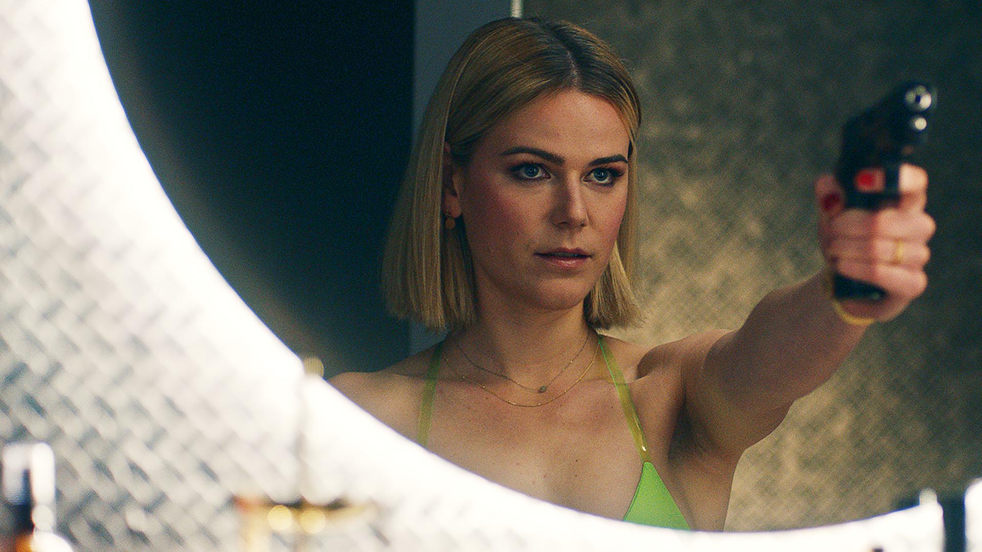 Franzi (Llewellyn Reichman) posiert mit Knarre vor dem Badezimmer Spiegel. | Comedy-Serie "Deadlines"