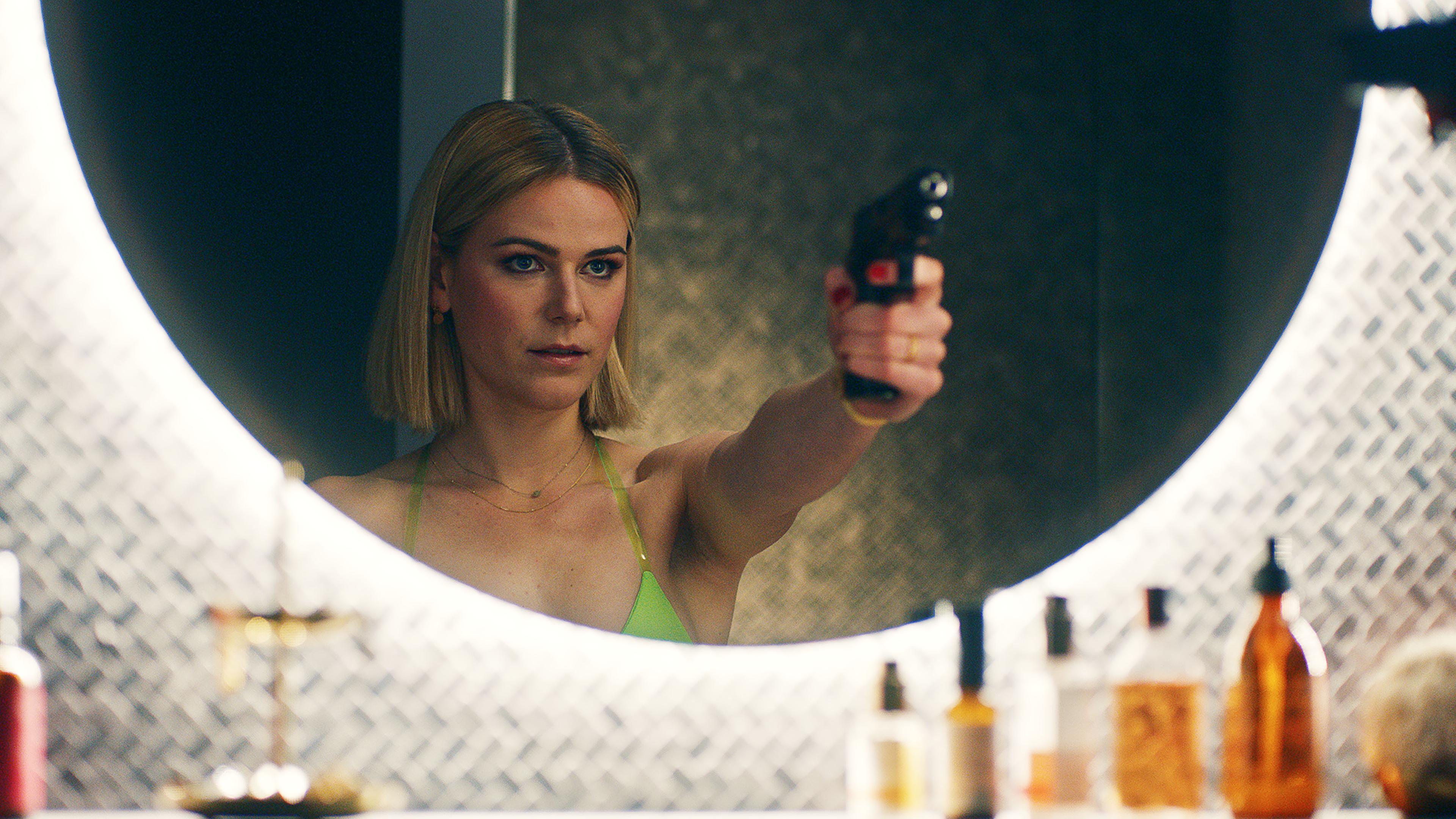 Franzi (Llewellyn Reichman) posiert mit Knarre vor dem Badezimmer Spiegel. | Comedy-Serie "Deadlines"