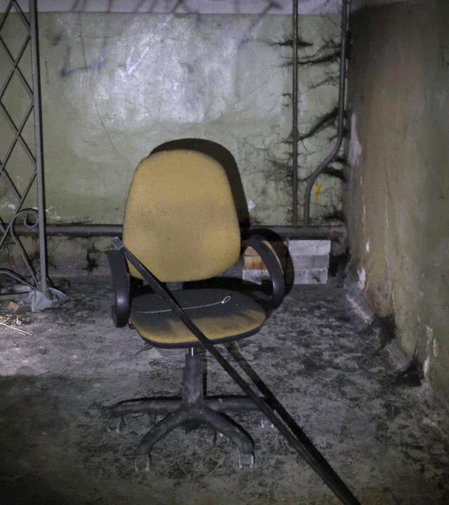 Stuhl, auf dem eine Eisenstange liegt, steht in dreckigem Kellerraum.