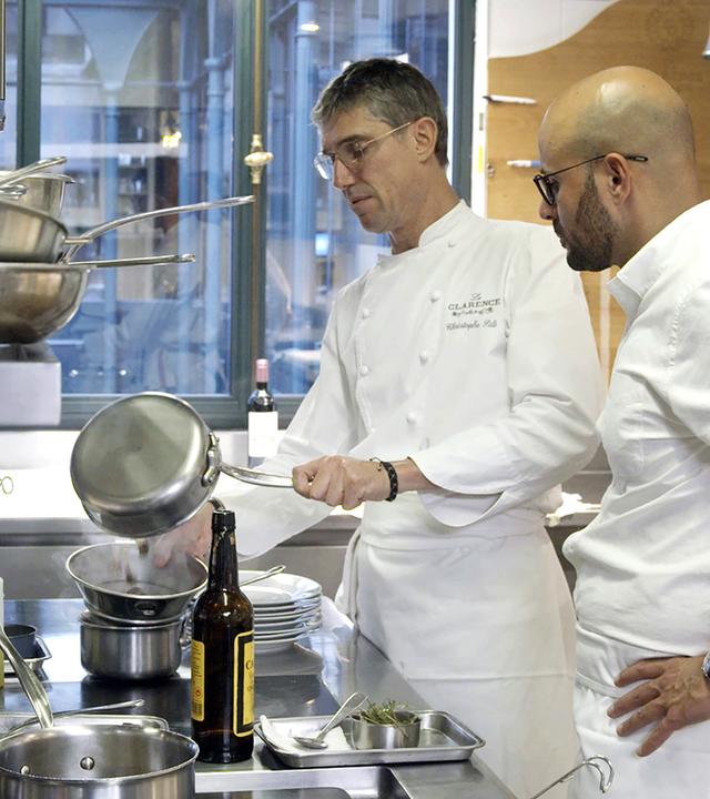 Zwei Männer, Carlton McCoy und Christophe Pelé, stehen mit Küchenuniform in der Küche am Herd und bereiten Essen zu.