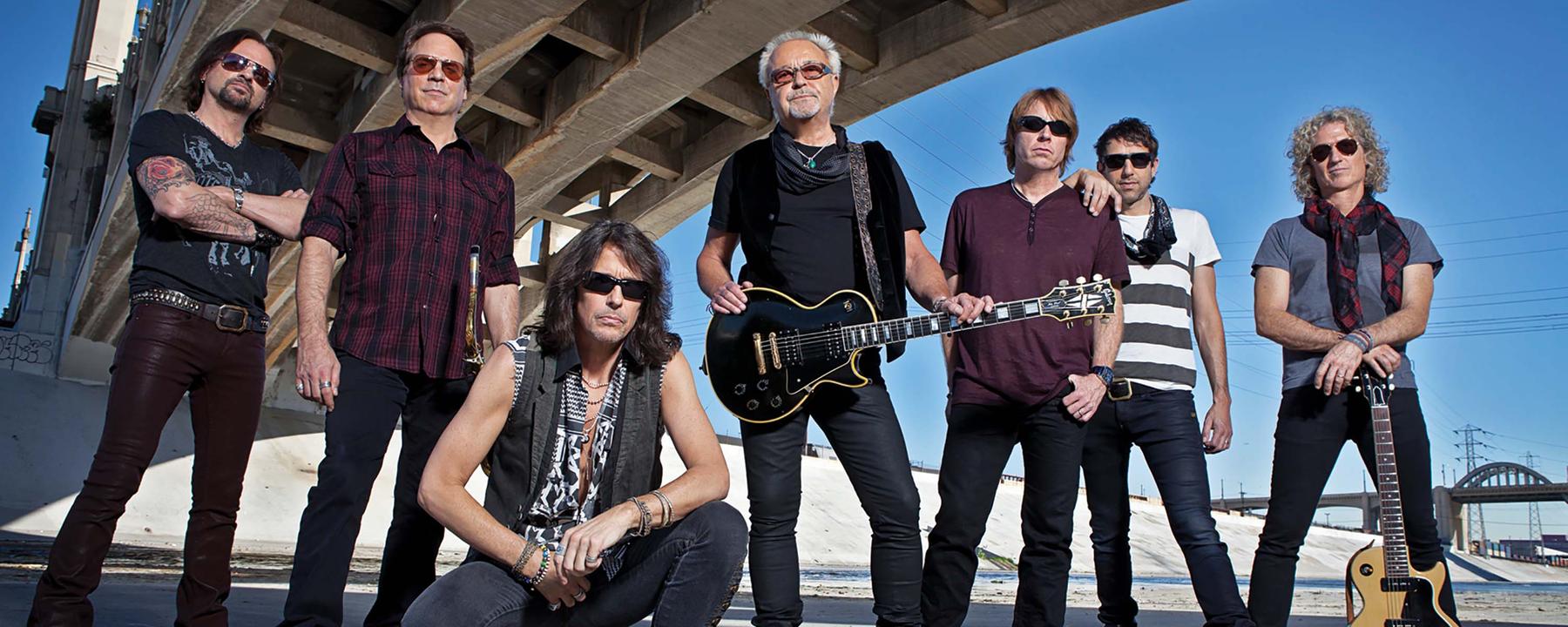 Die siebenköpfige Band Foreigner steht unter einer Brücke. Alle gekleidet mit schwarzen Hosen und T-Shirts.