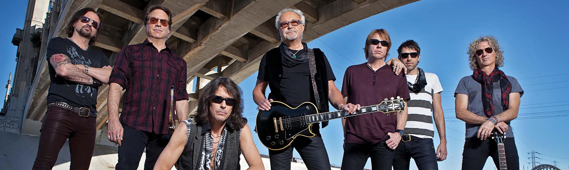 Die siebenköpfige Band Foreigner steht unter einer Brücke. Alle gekleidet mit schwarzen Hosen und T-Shirts.