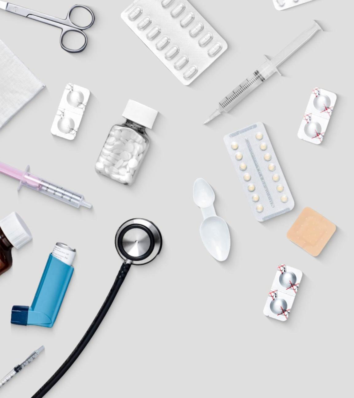 Das Bild zeigt den Schreibtisch eines Arztes oder einer Ärztin. Zu sehen sind etwa Tablettenverpackungen, zwei Spritzen und ein Asthma-Spray, aber auch eine Patienten-Akte.