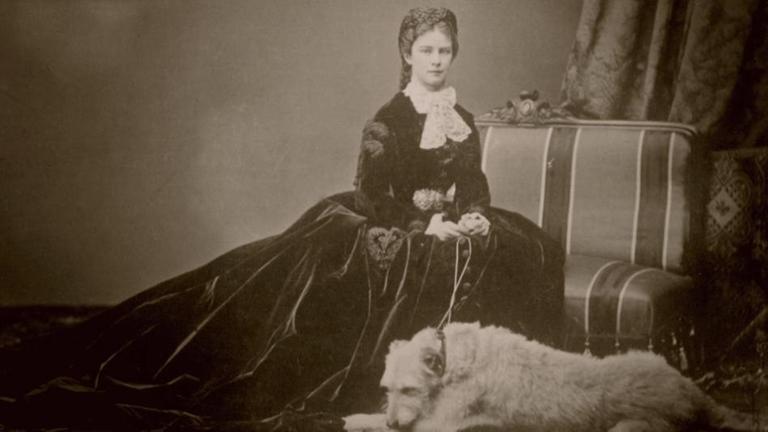 Foto von Kaiserin Sisi auf einem Polstersessel sitzend und ihrem Hund vor ihr liegend